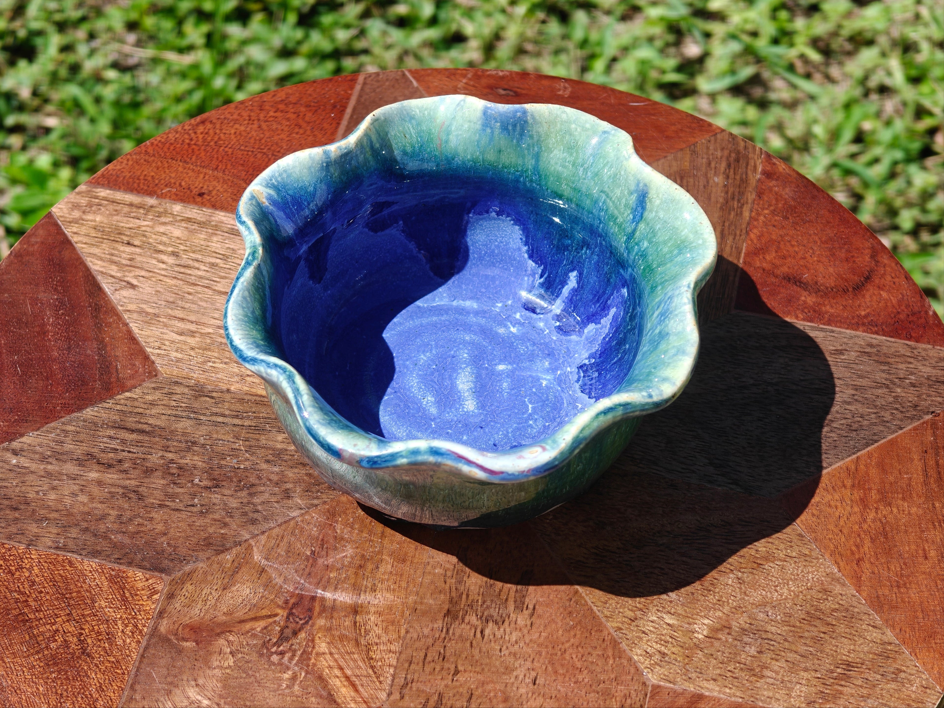 Blue ceramic pot on a wooden surface with grass in the background